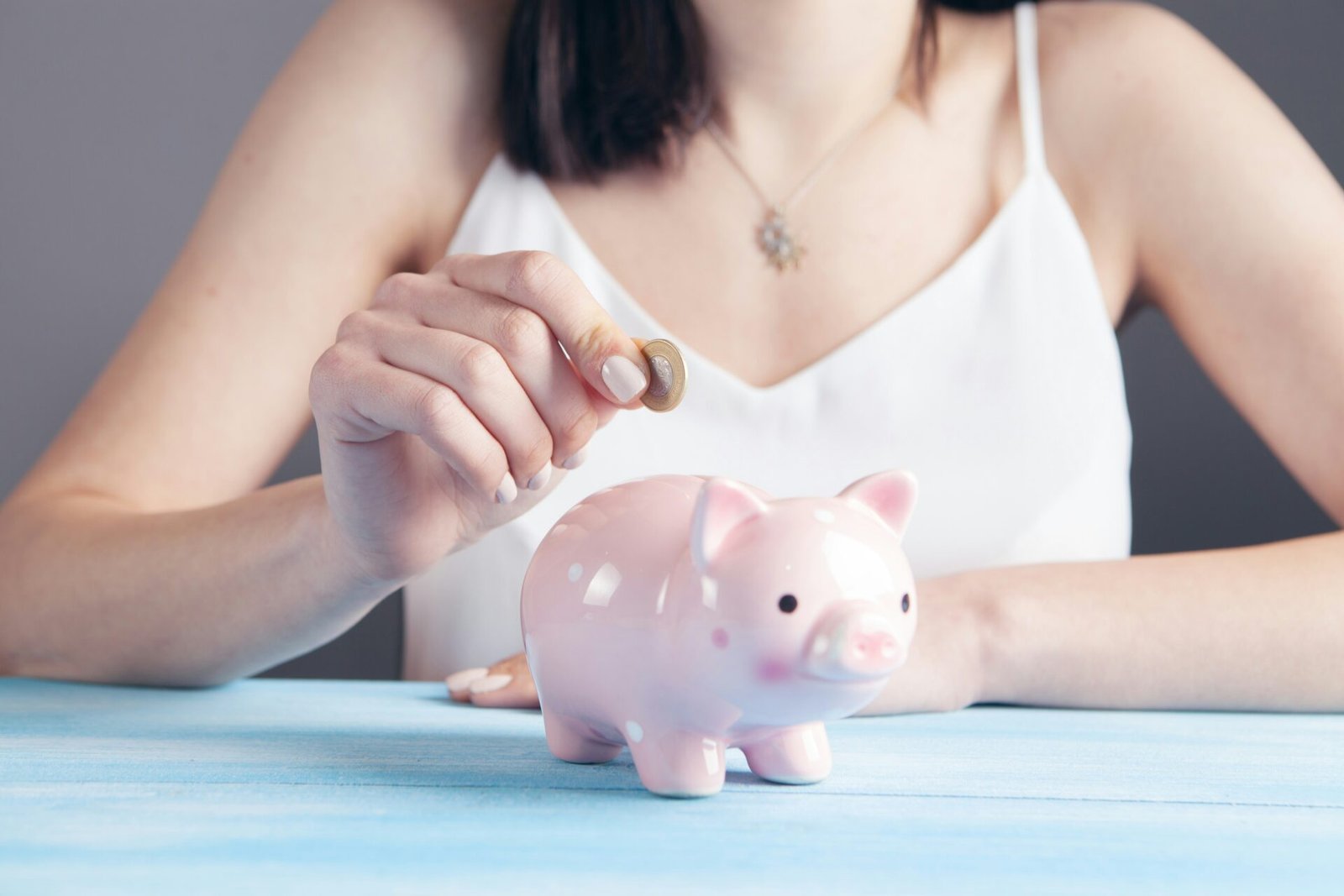 A woman inserting a coin into a pink piggy bank, symbolising saving money, budgeting and financial planning - best budgeting apps 2026