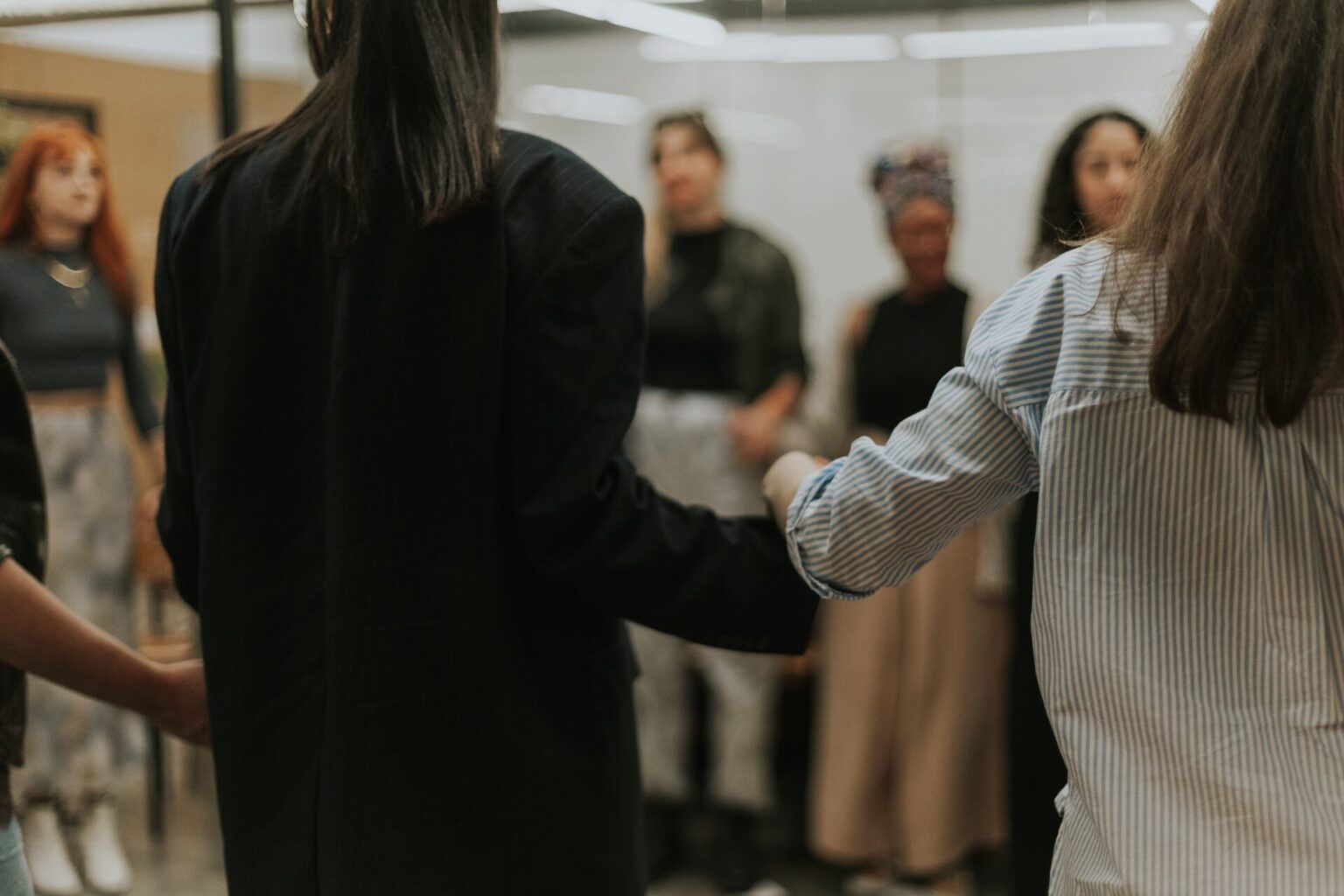 A group of women standing in a circle holding hands during a women-only club meeting, creating a safe social space for connection and community.
